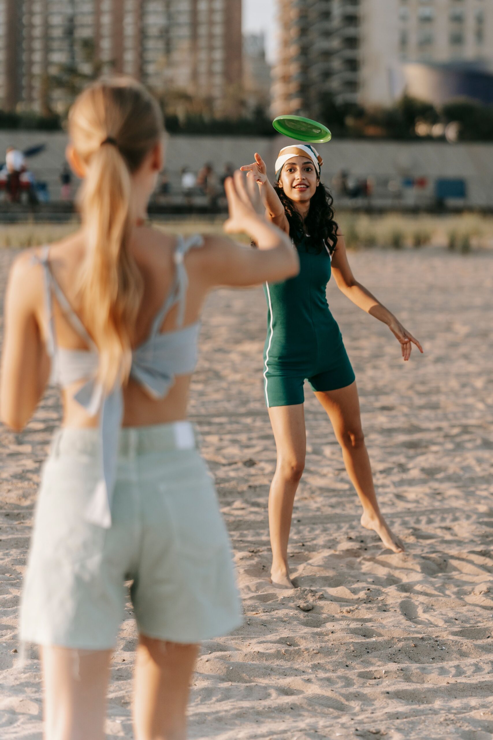 Two women enjoying a frisbee game on a sunny beach, embracing summer fun.